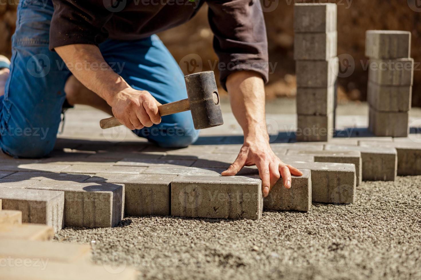 ung man om grå betong stenläggning plattor i hus gård på grus fundament bas. bemästra lägger stenläggning stenar. trädgård tegel väg stenläggning förbi professionell utläggare arbetstagare. reparation trottoar. foto