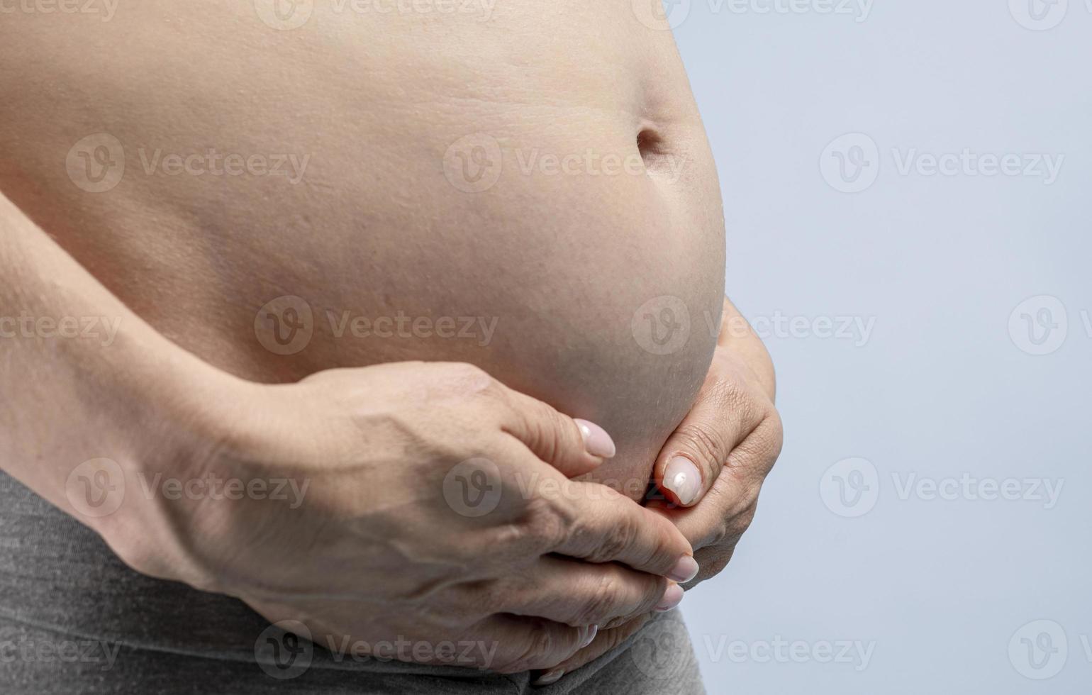 gravid kvinna innehar händer på mage på en blå bakgrund. graviditet, moderskap, förberedelse och förväntan begrepp. närbild, inomhus. skön foto