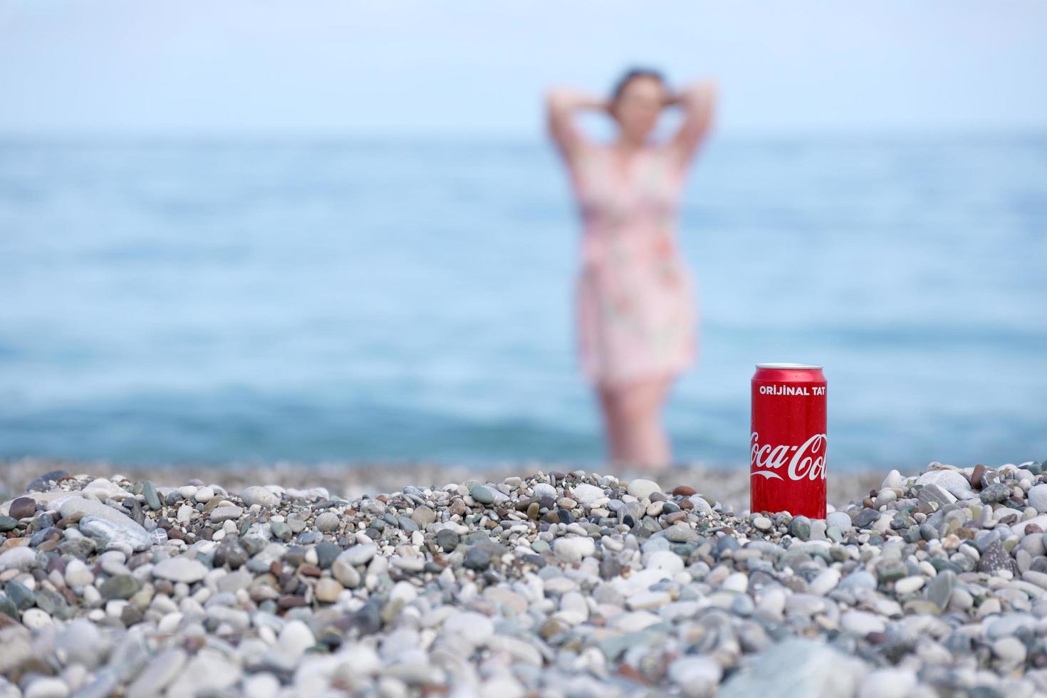 antalya, Kalkon - Maj 18, 2022 original- coca cola röd tenn kan lögner på små runda sten stenar stänga till hav Strand. Coca Cola kan och kvinna på strand foto