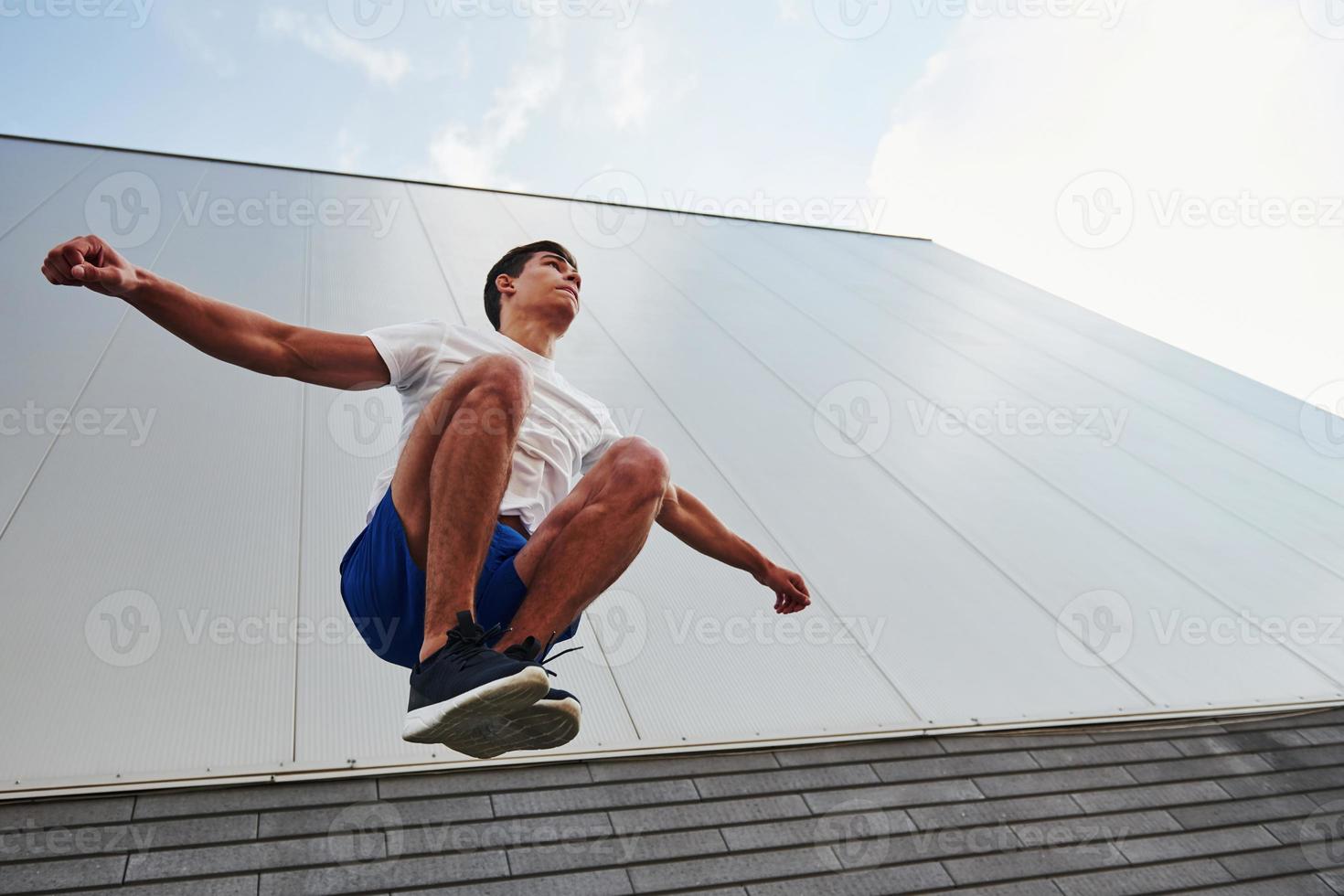 in i de luft. ung sporter man håller på med parkour i de stad på solig dagtid foto