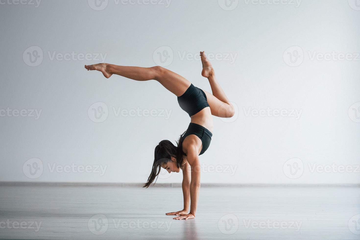 håller på med hand stå. ung sportig kvinna i svart kläder med smal kropp typ i de friska Centrum håller på med övningar foto