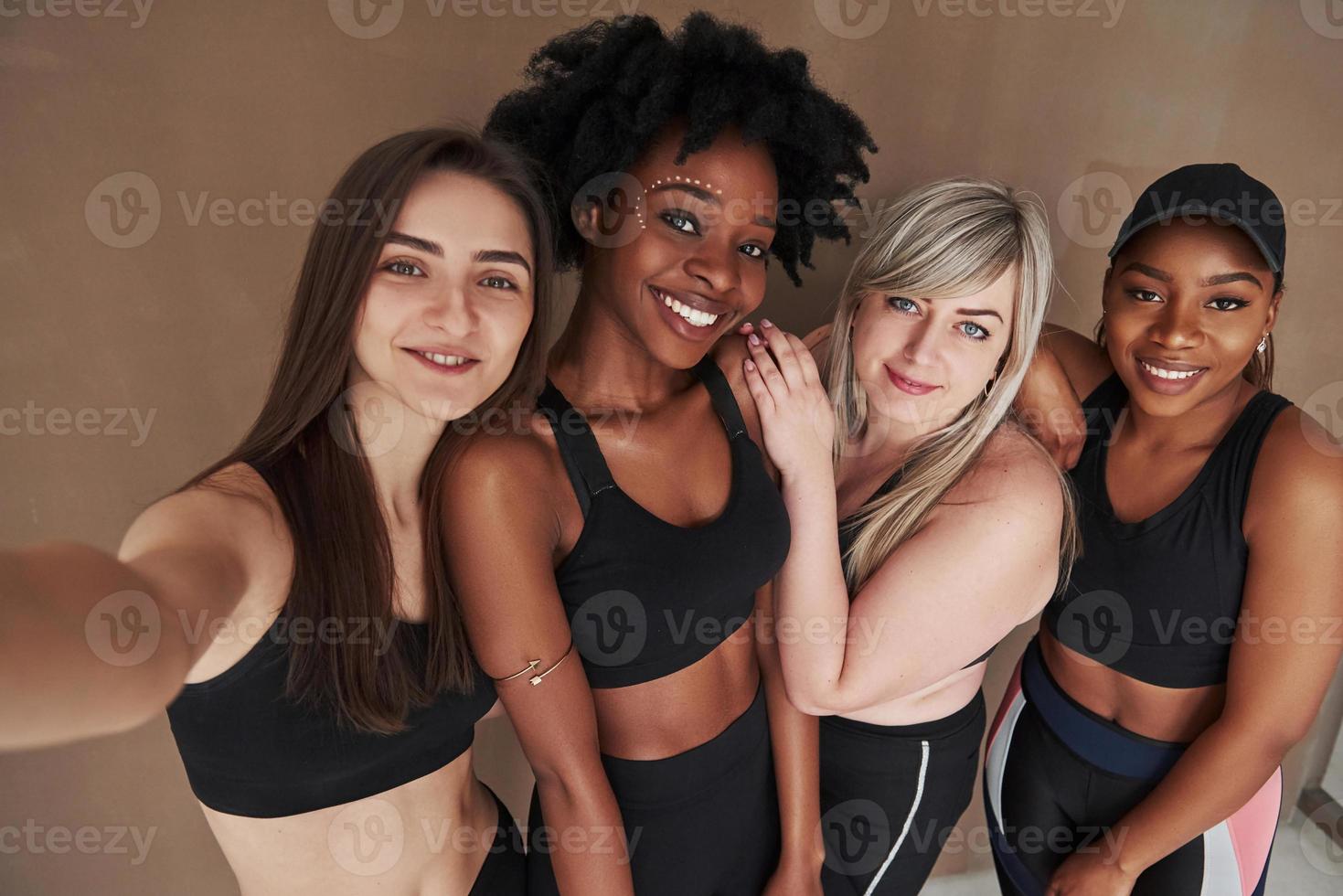 snälla le mot kameran. grupp av multietniska kvinnor står i studion mot brun bakgrund foto