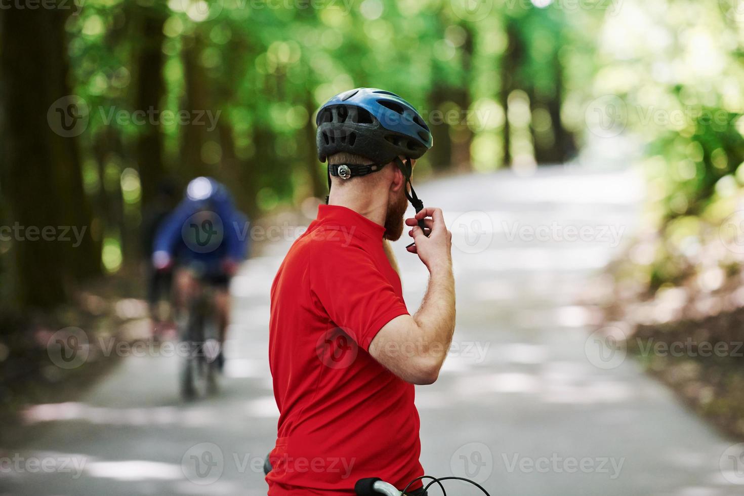 bär skyddshjälm. cyklist på en cykel är på asfaltvägen i skogen på en solig dag foto