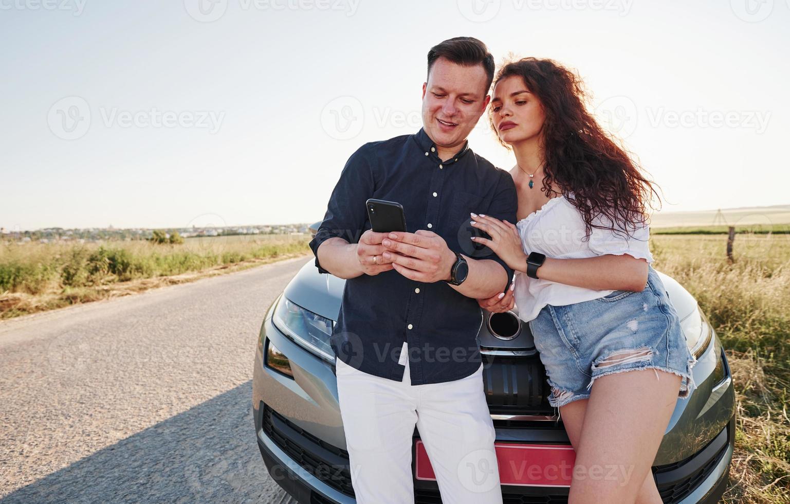 använder sig av smartphone. härlig par nära deras ny modern bil på helgen tid foto