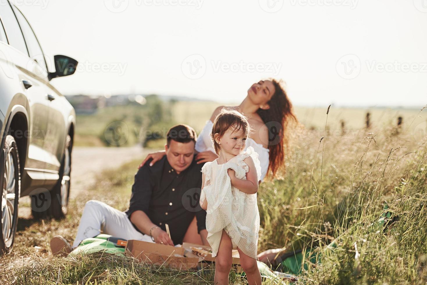 hög gräs. familj ha picknick på landsbygden nära silver- bil på solnedgång foto