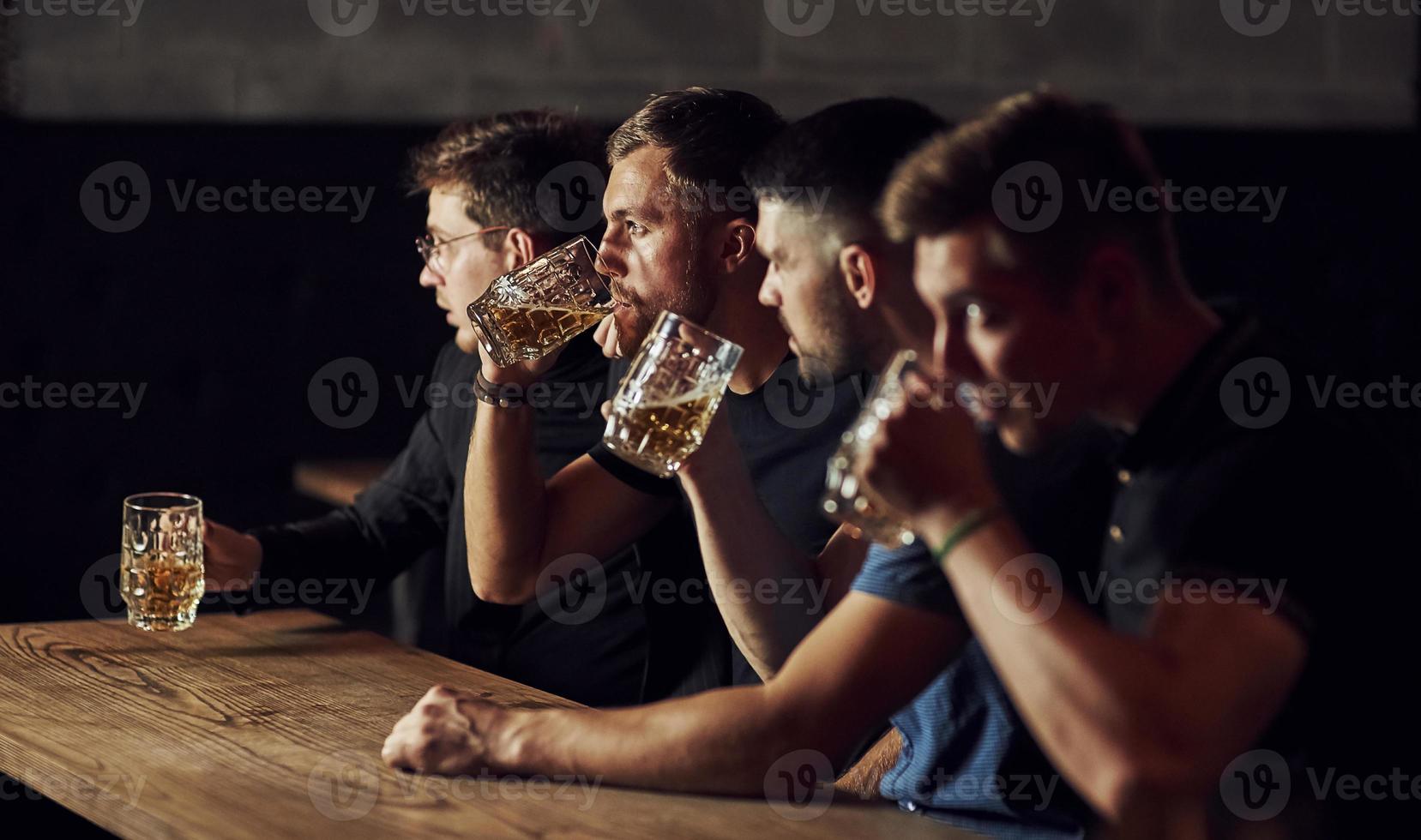 dricka öl. tre sporter fläktar i en bar tittar på fotboll foto