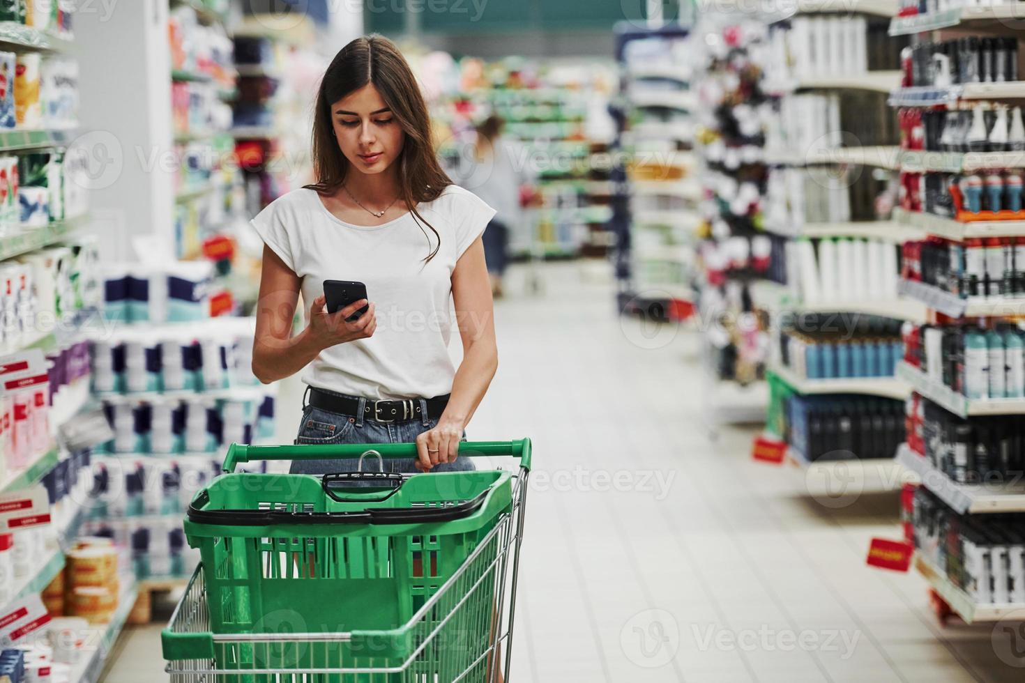 använder sig av smartphone. kvinna shopper i tillfällig kläder i marknadsföra ser för Produkter foto