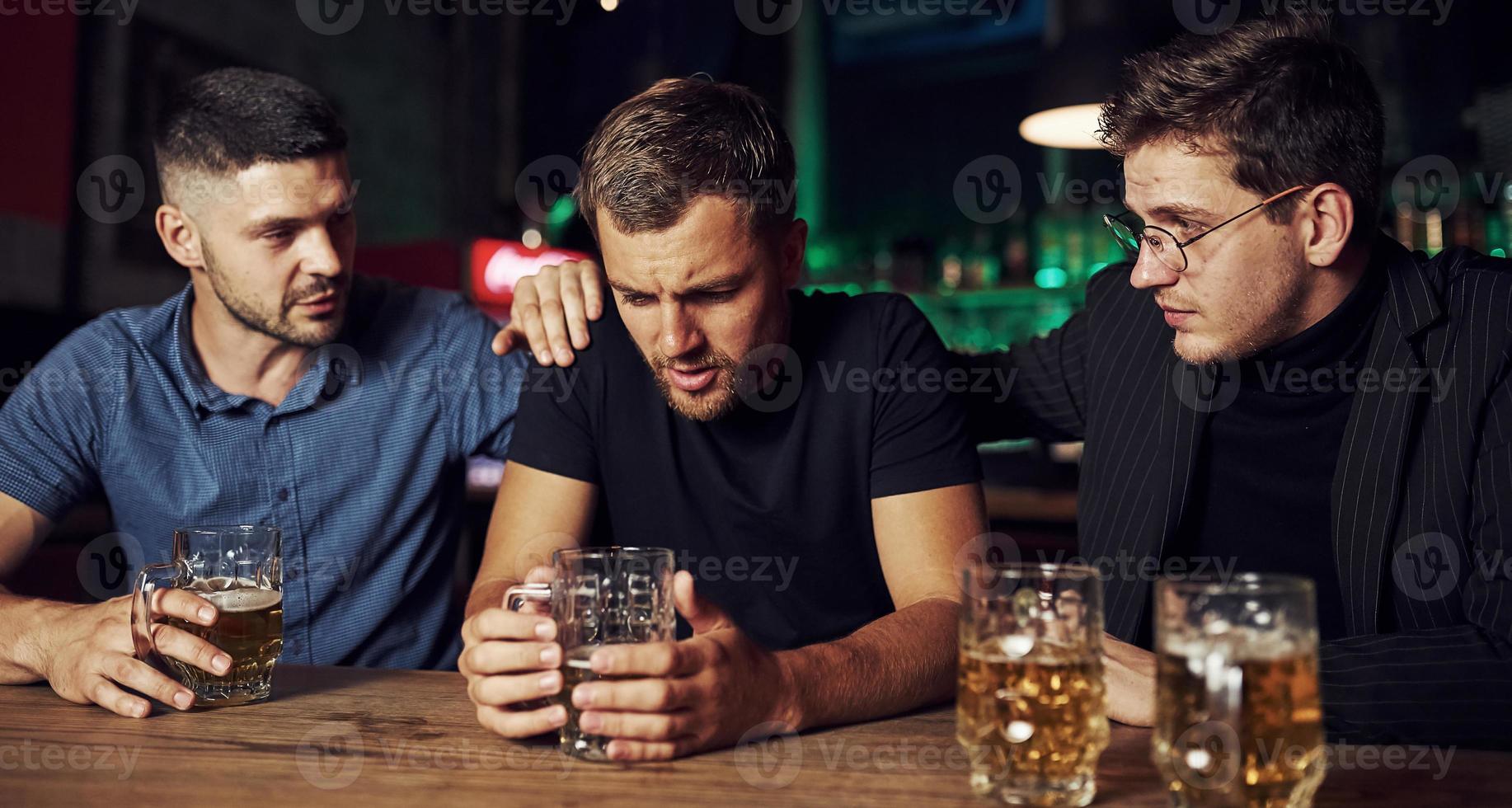 tre manlig vänner i de bar. stödjande ledsen vän. enhet av människor. med öl på de tabell foto