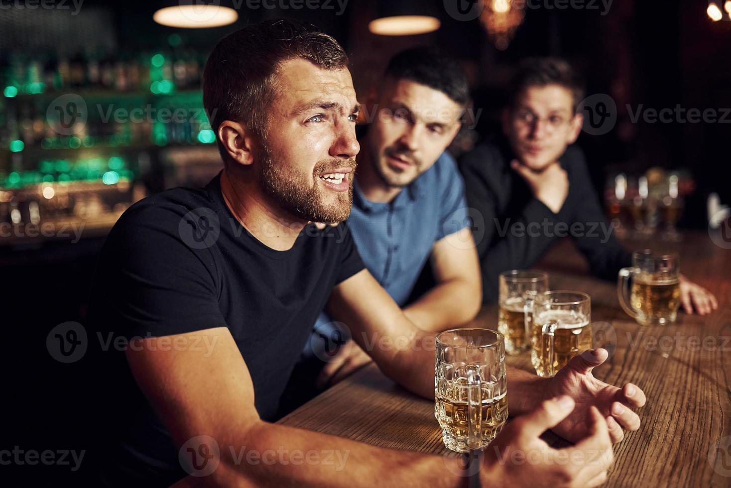 tre manlig vänner i de bar. stödjande ledsen vän. enhet av människor. med öl på de tabell foto