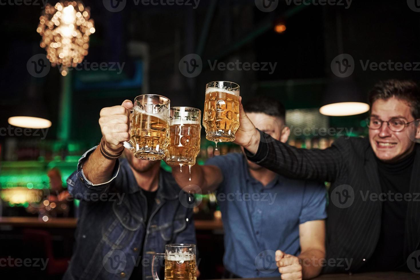 knackar glasögon. tre sporter fläktar i en bar tittar på fotboll. med öl i händer foto