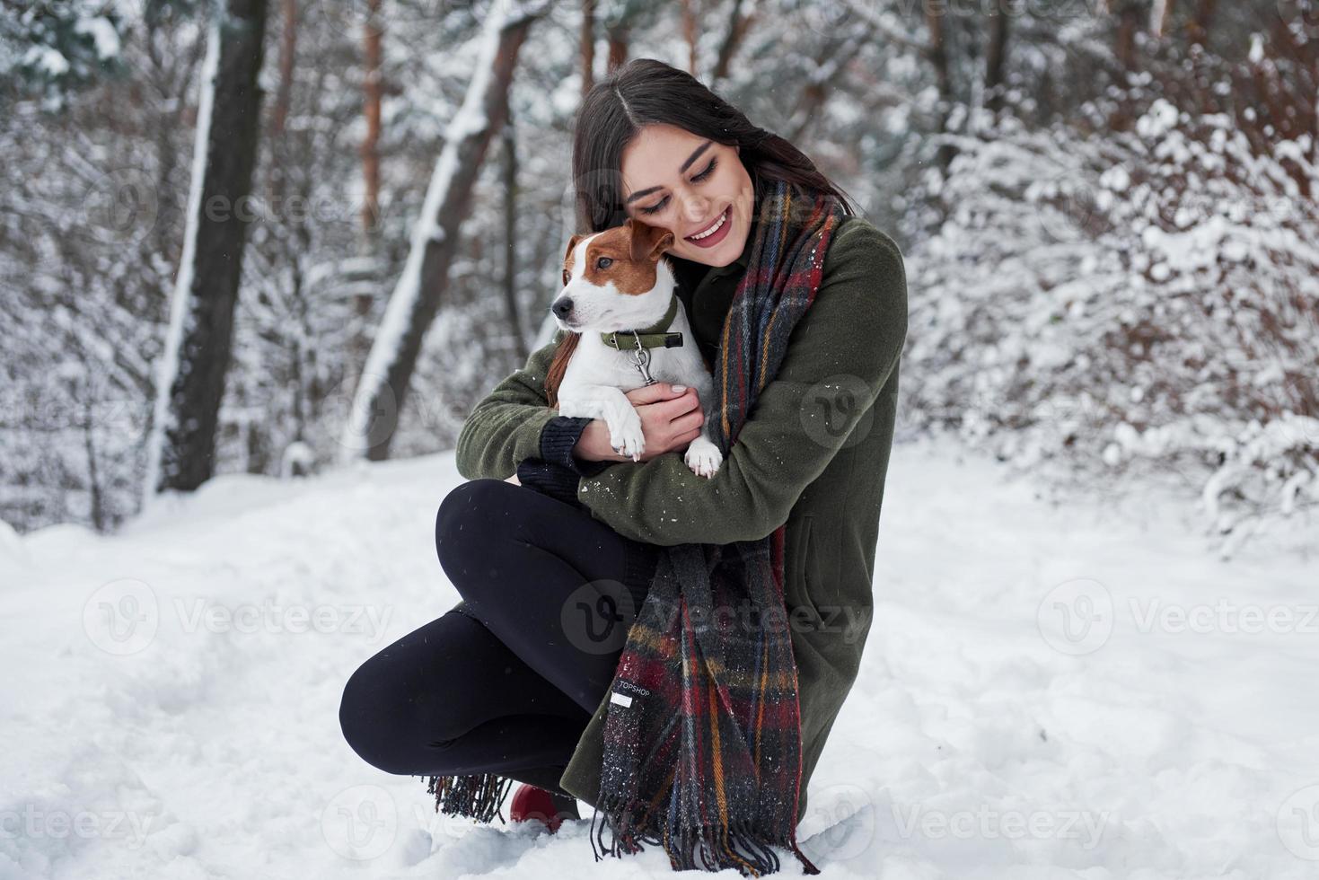 söt kramar. leende brunett har roligt medan gående med henne hund i de vinter- parkera foto