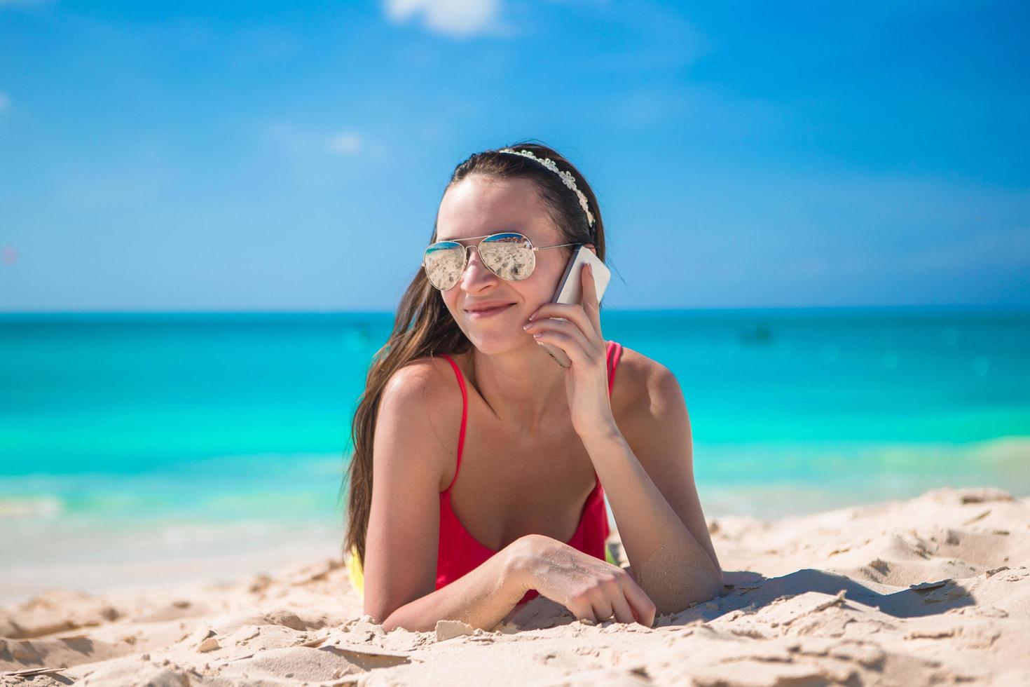 kvinna som ligger på stranden och pratar via sin telefon foto