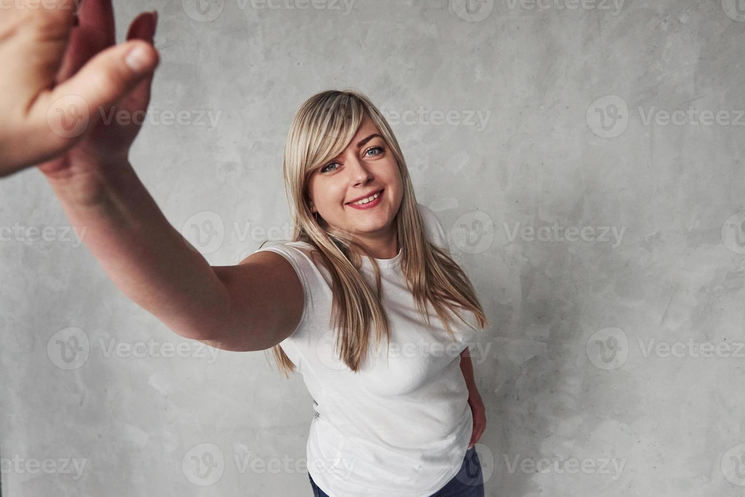 hälsningar till du. ung vit kvinna i de studio stående mot grå bakgrund foto