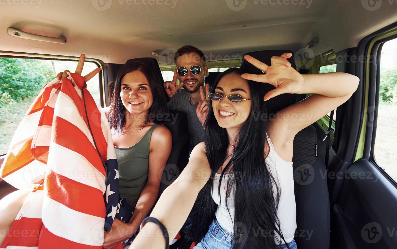 vänner framställning selfie när sitter inomhus med amerikan flagga i händer foto