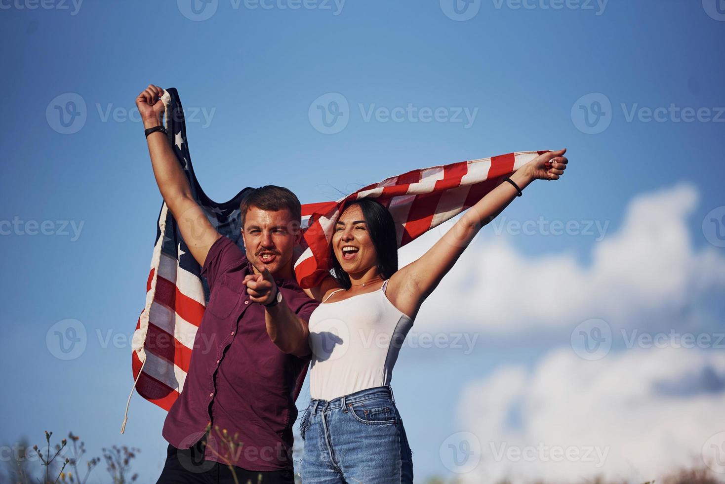 med händer upp. känner frihet. skön par med amerikan flagga ha en Bra tid utomhus i de fält foto