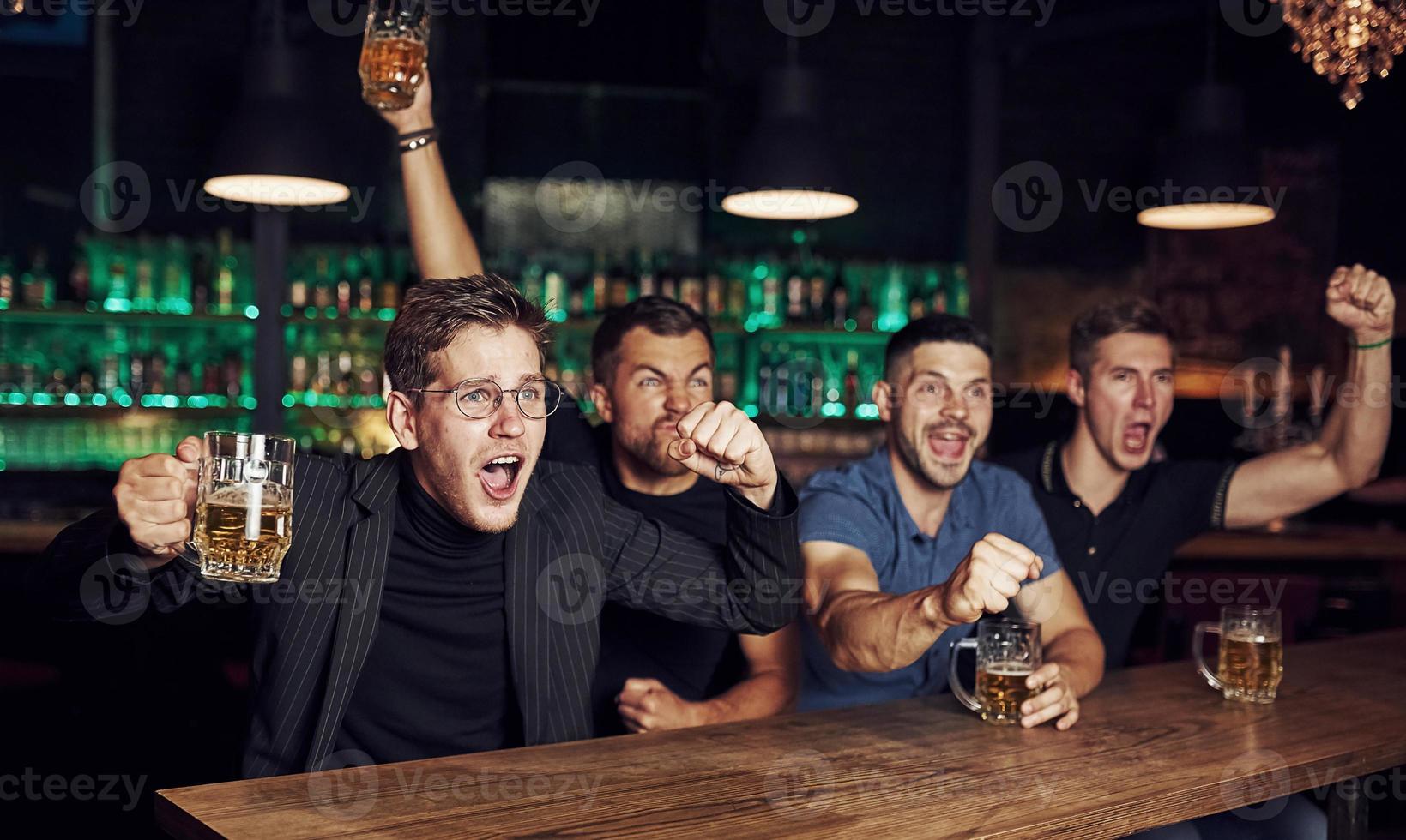 dess en mål. fira seger. tre sporter fläktar i en bar tittar på fotboll. med öl i händer foto