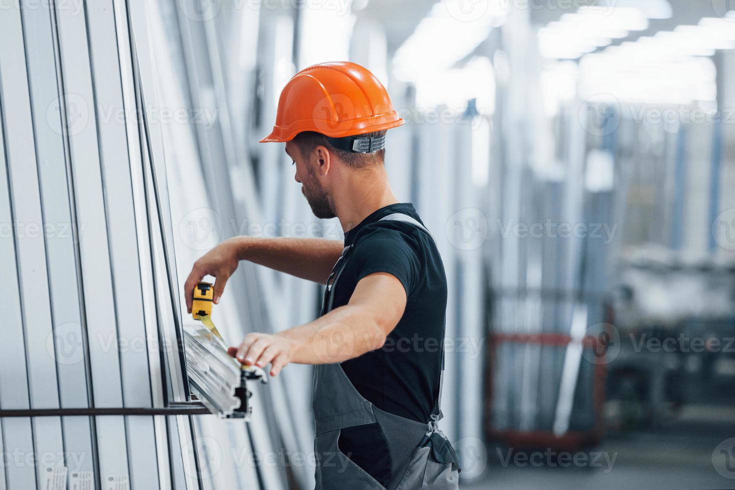 mätning längd av objekt. industriell arbetstagare inomhus i fabrik. ung tekniker med orange hård hatt foto