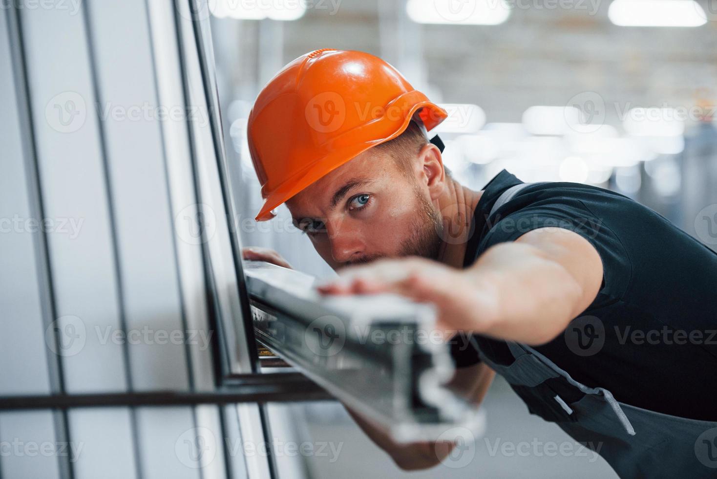 mätning längd av objekt. industriell arbetstagare inomhus i fabrik. ung tekniker med orange hård hatt foto