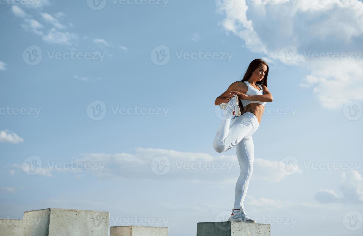 på de cement kub. skott av sportigt kvinna håller på med kondition övningar nära de sjö på dagtid foto