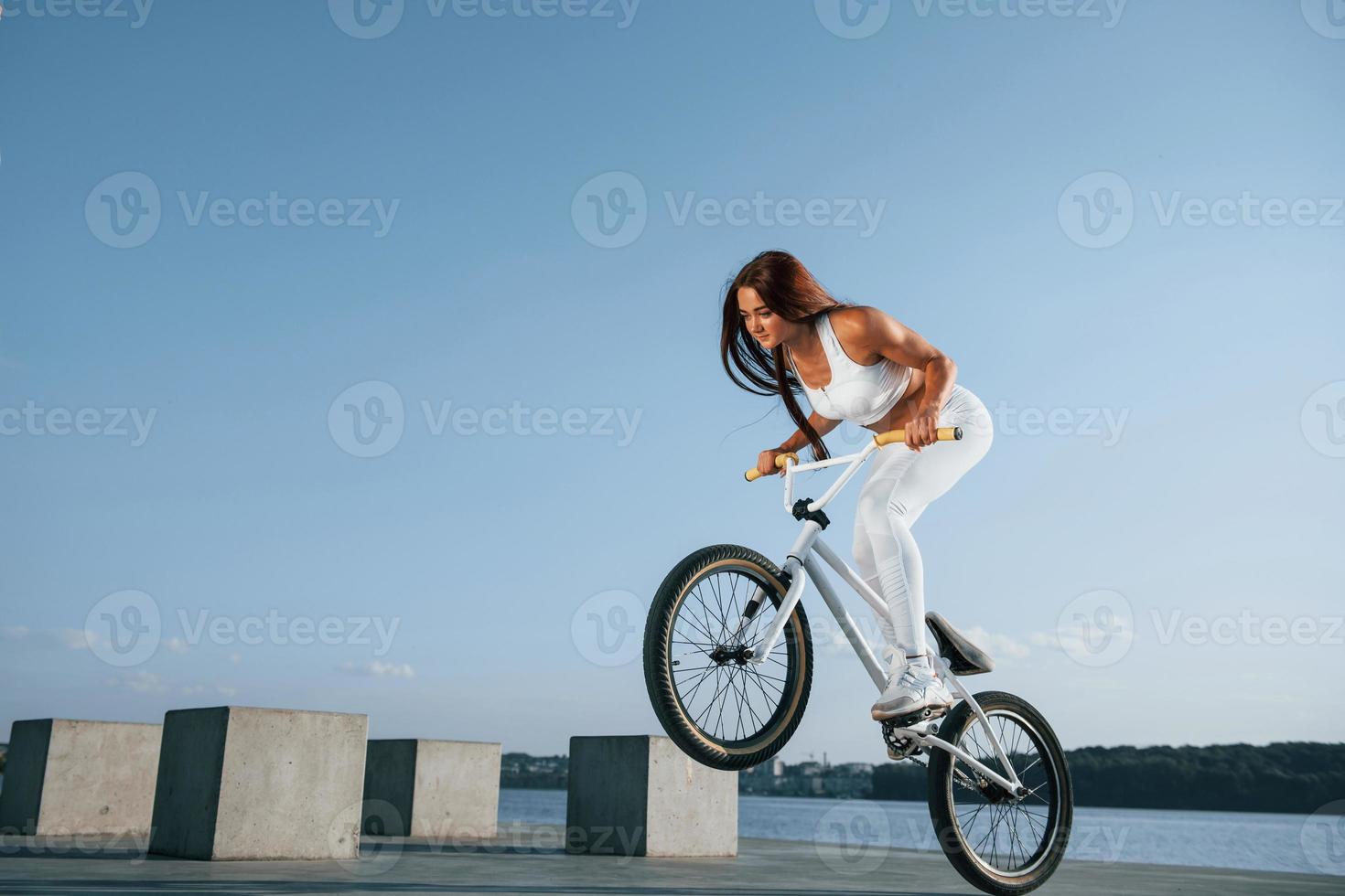 håller på med stunts. kvinna ryttare är på de cykel på dagtid nära de sjö. kondition kvinna i sportigt kläder foto