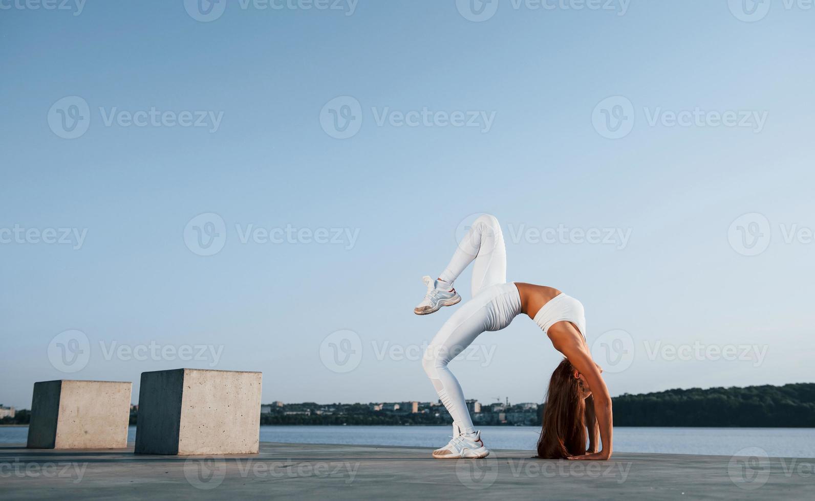 skott av sportig kvinna som gör fitnessövningar nära sjön på dagtid foto