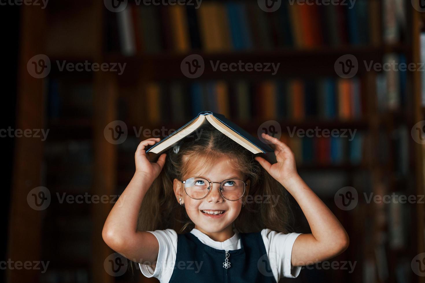 söt liten flicka i glasögon står i de bibliotek full av böcker. uppfattning av utbildning foto