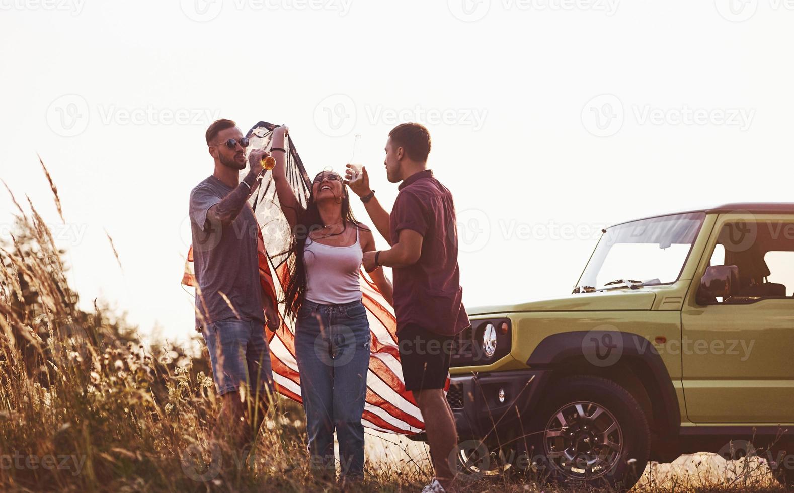 har konversation. vänner ha trevlig helgen utomhus nära deras grön bil med USA flagga foto