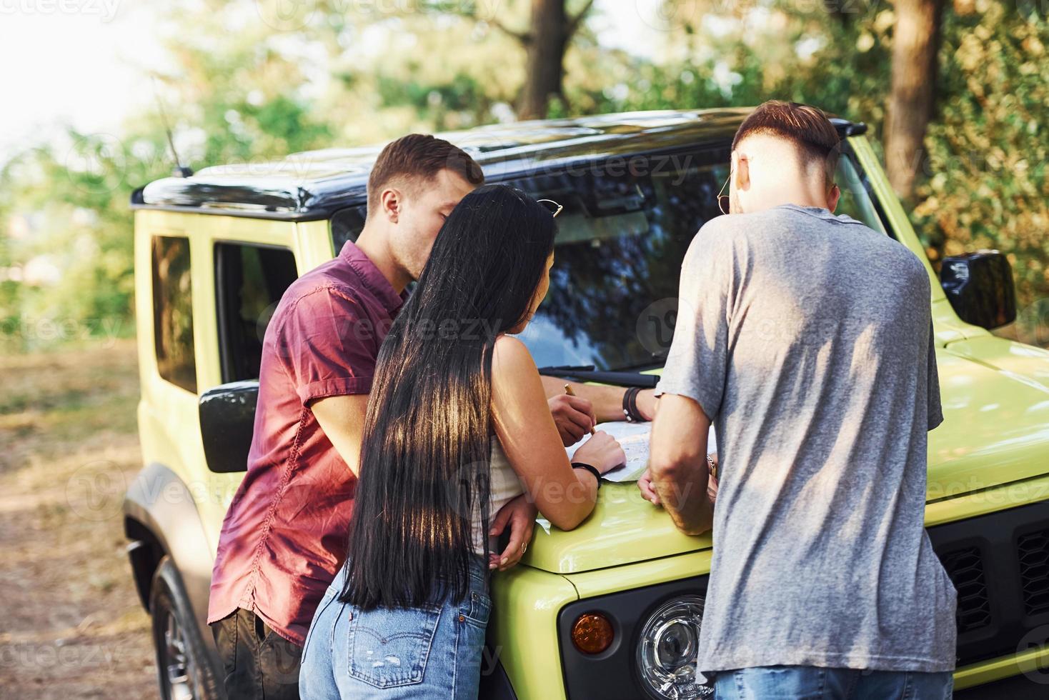 ung vänner läsning Karta den där är på de huva av modern grön jeep i de skog foto