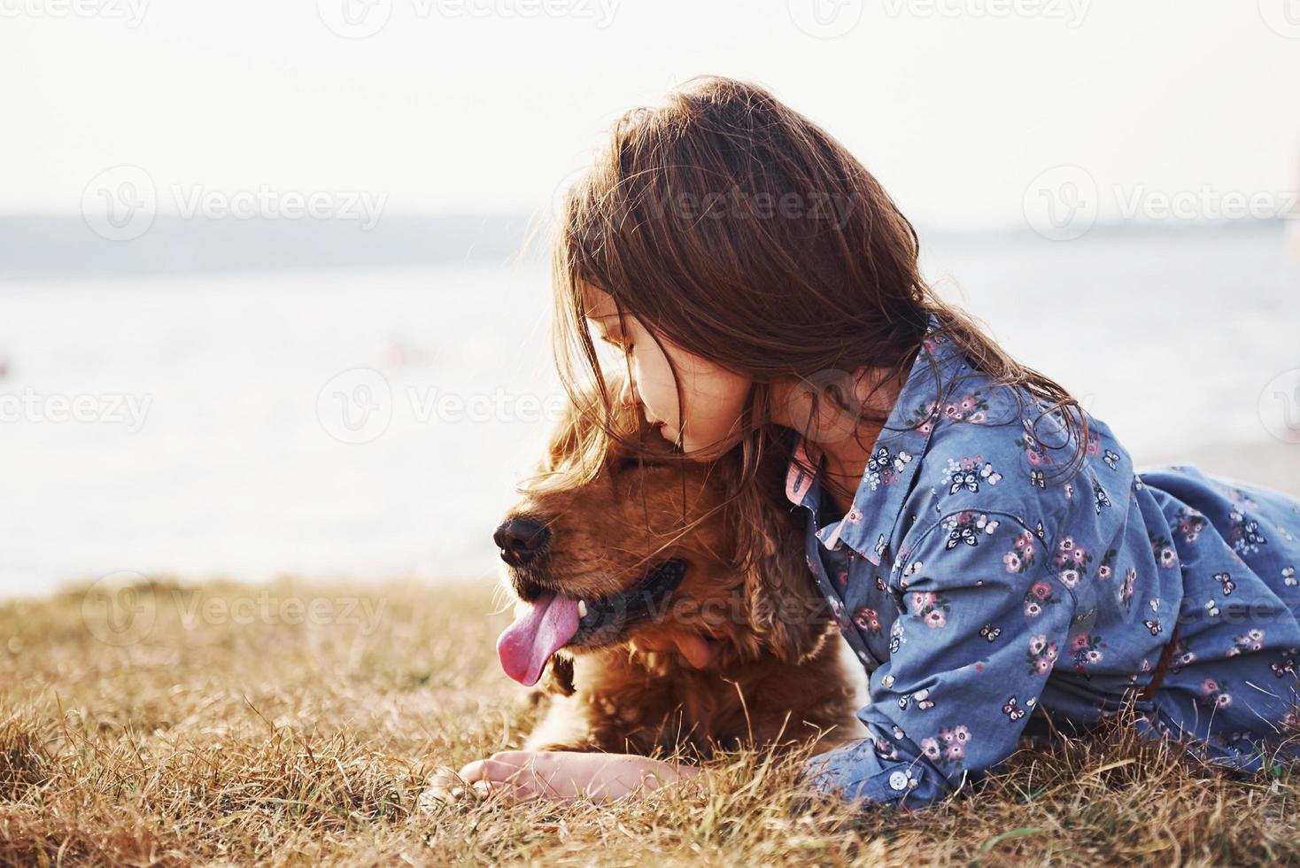 vilar nära de sjö. söt liten flicka ha en promenad med henne hund utomhus på solig dag foto