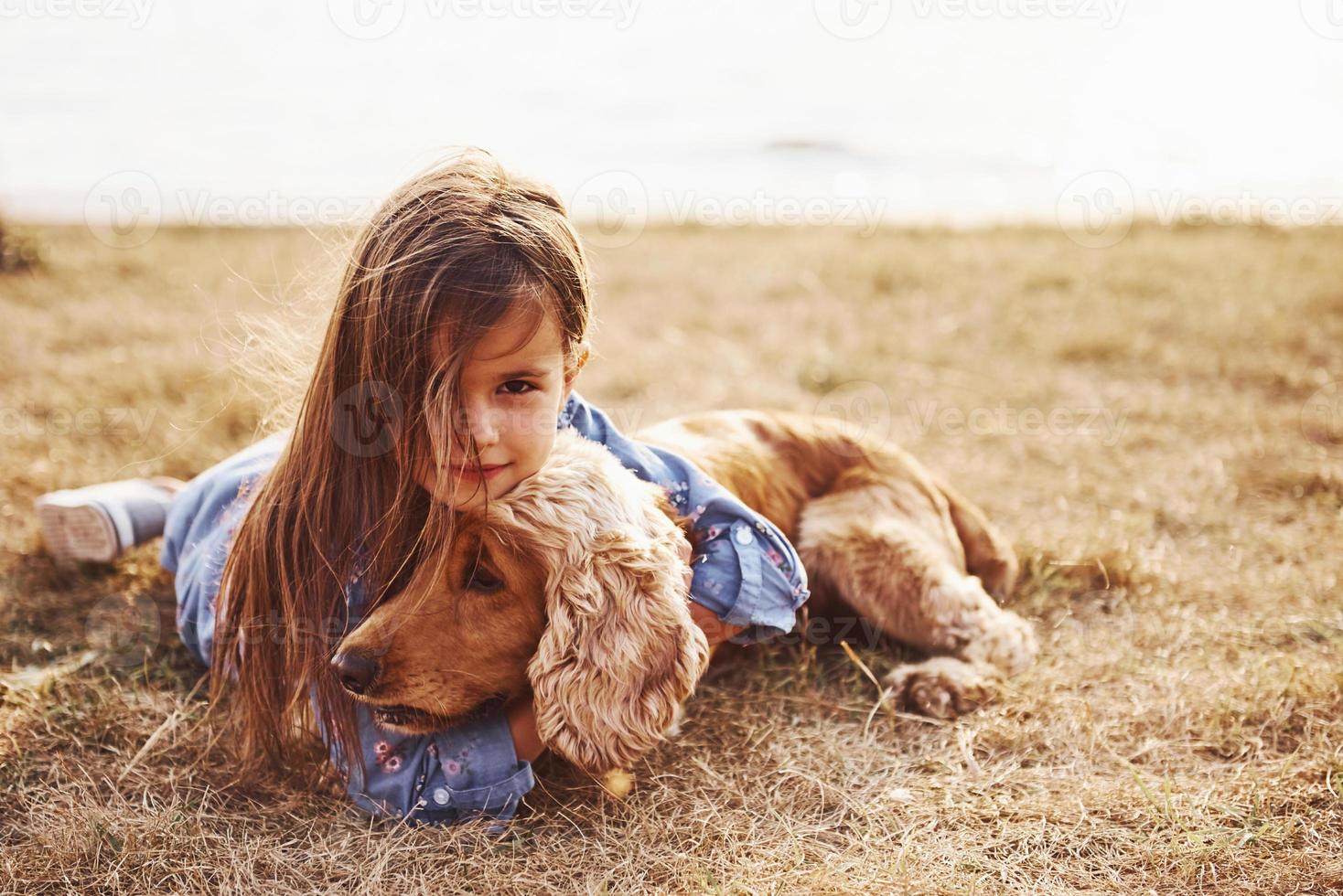 vilar nära de sjö. söt liten flicka ha en promenad med henne hund utomhus på solig dag foto