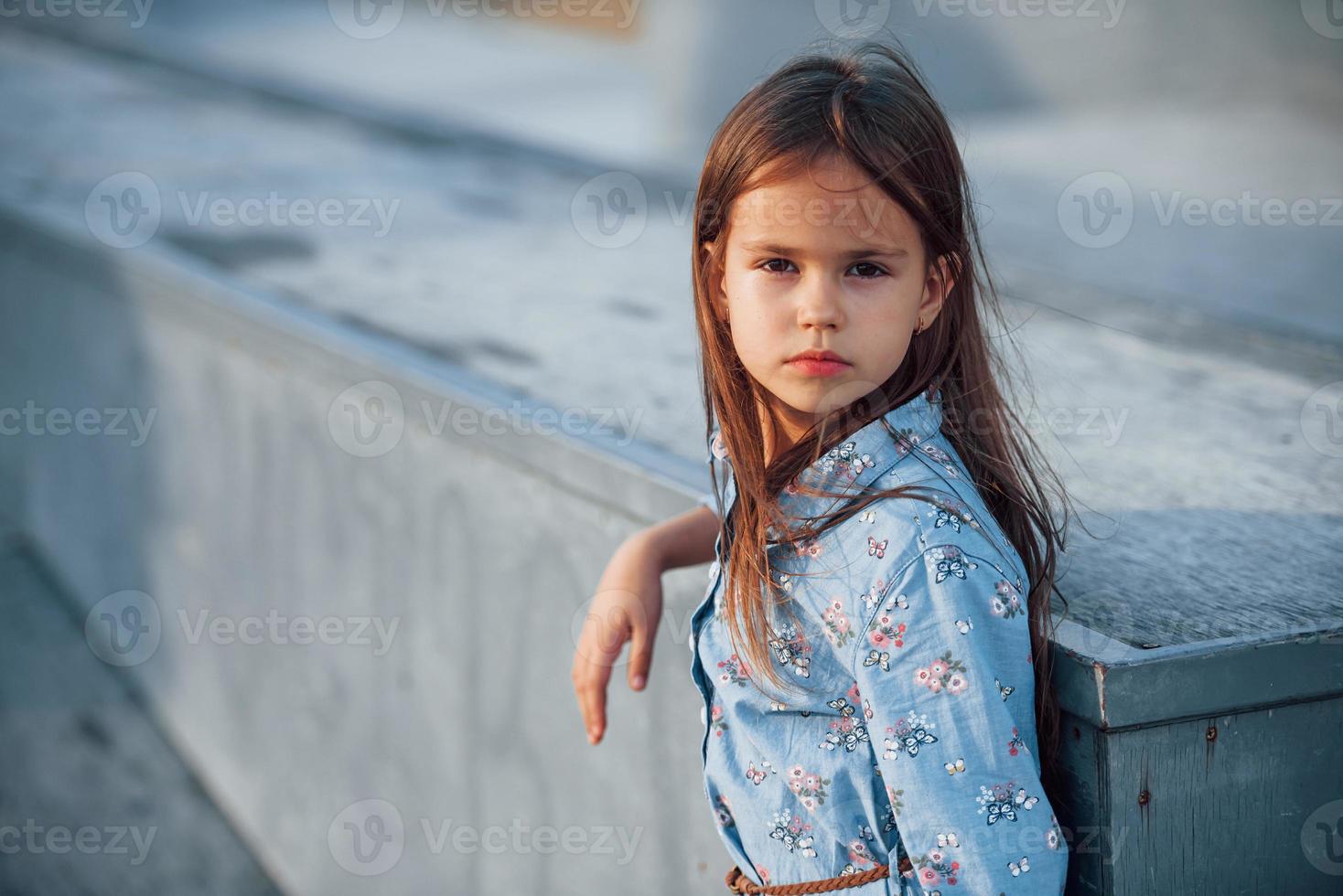 liten flicka i blå ha på sig Framställ för en kamera i de stad när lutande på de ramp foto