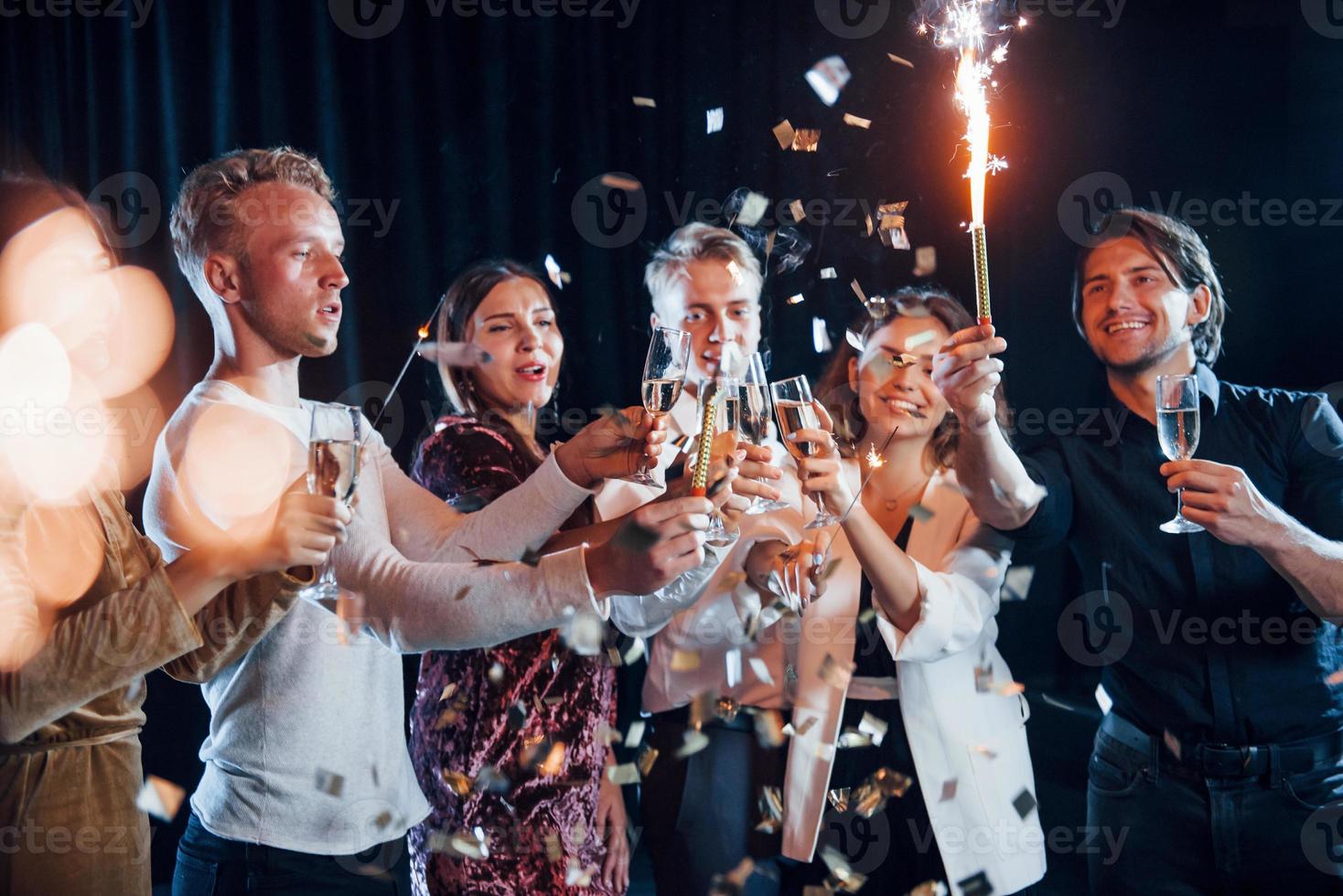 knackar glasögon. grupp av glad vänner fira ny år inomhus med drycker i händer foto