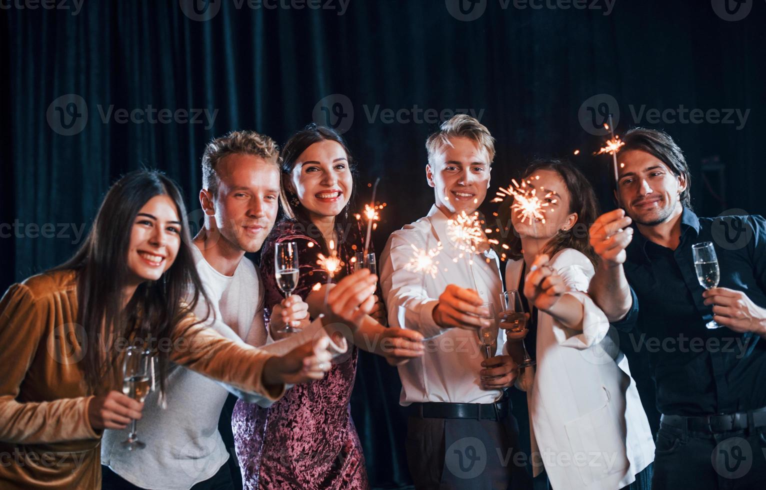 har roligt med tomtebloss. grupp av glad vänner fira ny år inomhus med drycker i händer foto