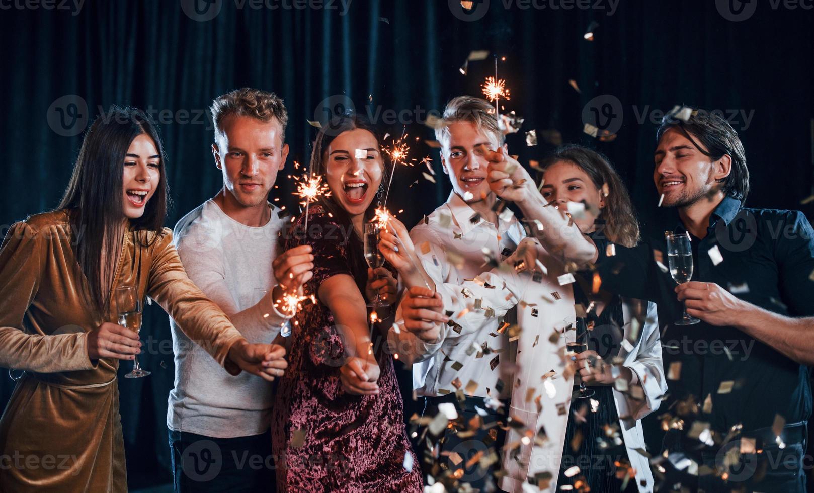 har roligt med tomtebloss. grupp av glad vänner fira ny år inomhus med drycker i händer foto