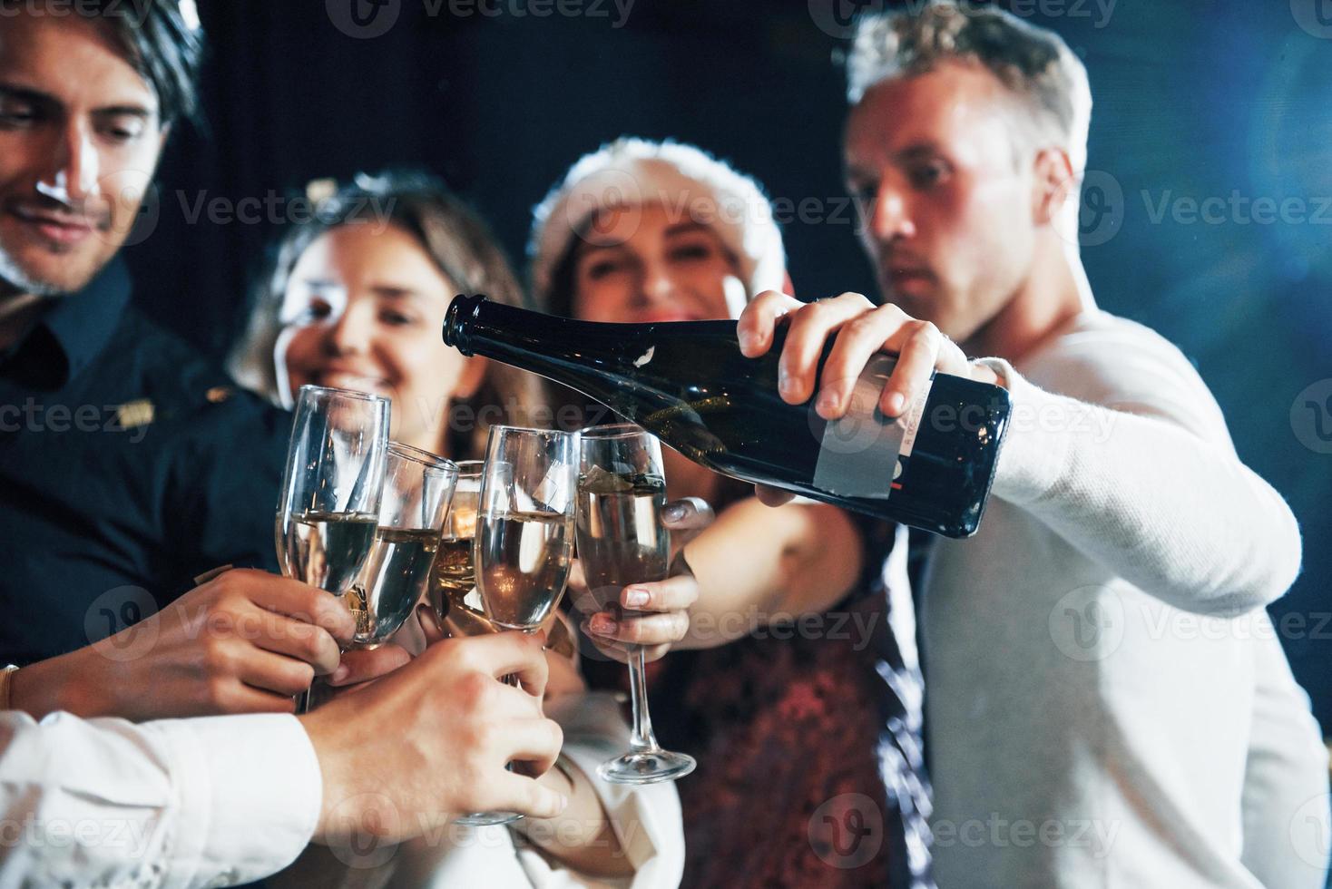 häller champagne. grupp av glad vänner fira ny år inomhus med drycker i händer foto