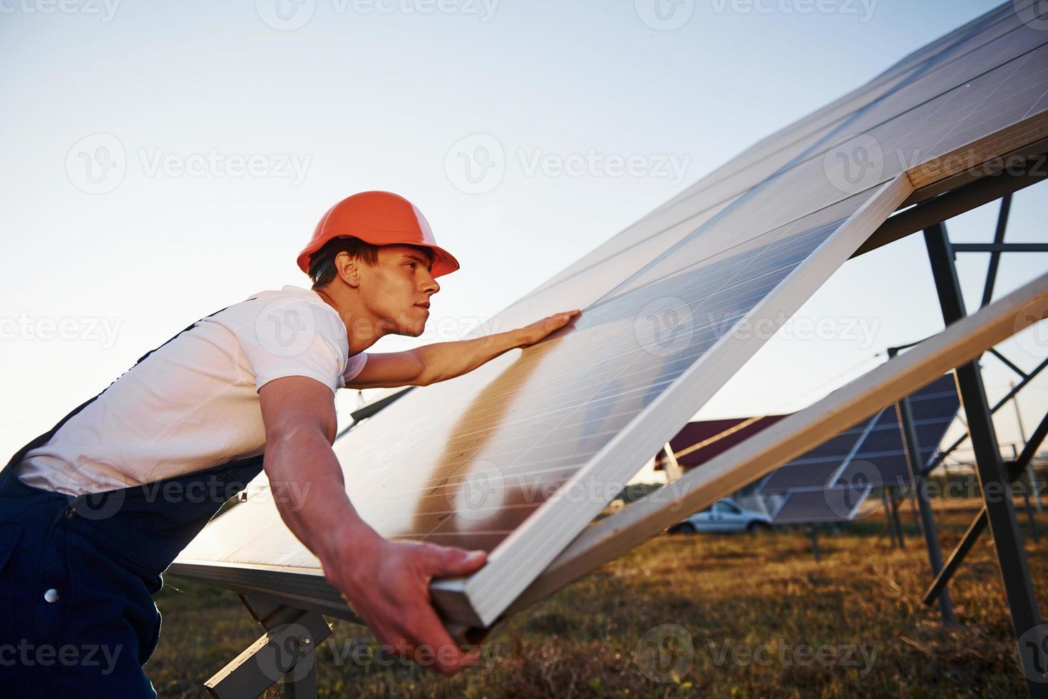 manuell arbete. manlig arbetstagare i blå enhetlig utomhus med sol- batterier på solig dag foto