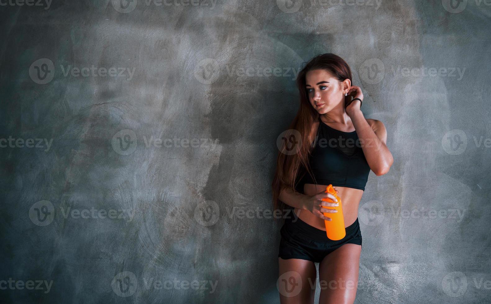 ung kondition kvinna med smal typ av kropp och flaska av vatten är lutande på de vägg foto
