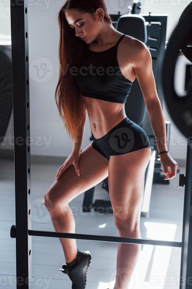 Framställ för de kamera. ung kondition kvinna med smal typ av kropp och i svart sportigt kläder är i de Gym foto