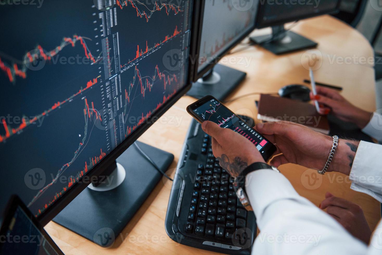 med telefon i händer. två aktiemäklare i formell kläder Arbetar i de kontor med finansiell marknadsföra foto