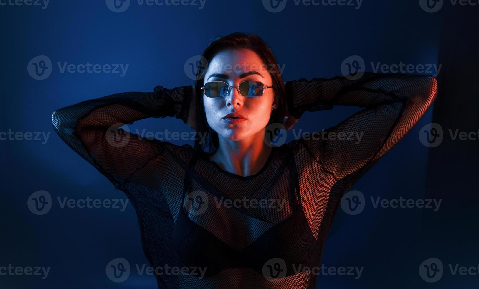 varm brunett i solglasögon Framställ i de studio med neon belysning foto