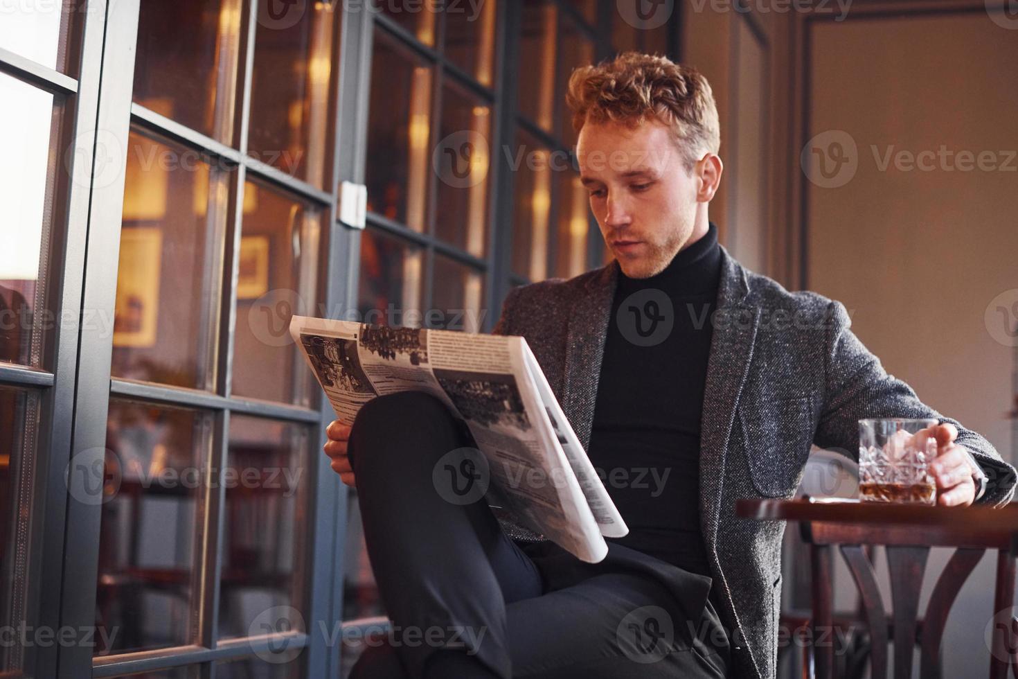 porträtt av modern ung kille i formell kläder den där sitter i de Kafé och läser tidning foto