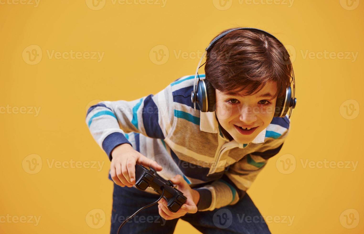 söt liten pojke spelar video spel i de studio mot gul bakgrund foto