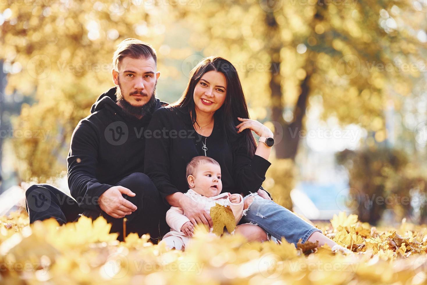 glad familj sitter på de jord och har roligt tillsammans med deras barn i skön höst parkera foto