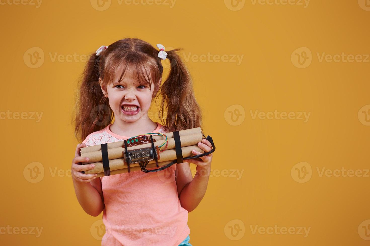 liten flicka med explosiv i de studio mot gul bakgrund foto