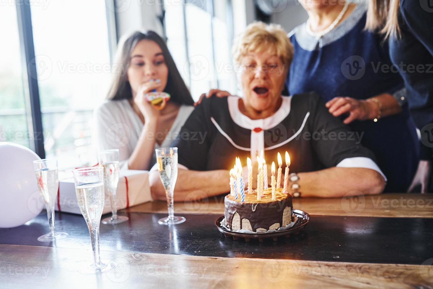 blåser de ljus. senior kvinna med familj och vänner fira en födelsedag inomhus foto