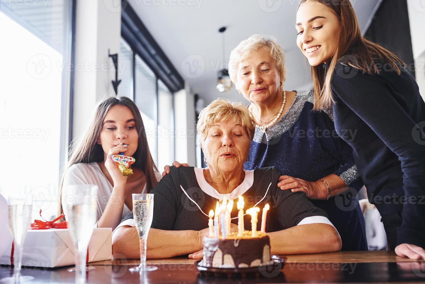 blåser de ljus. senior kvinna med familj och vänner fira en födelsedag inomhus foto