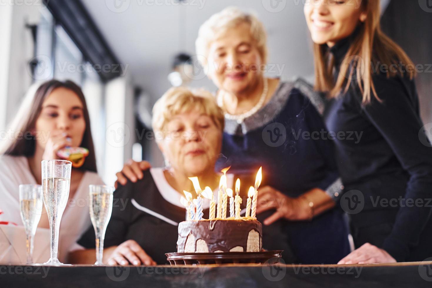 blåser de ljus. senior kvinna med familj och vänner fira en födelsedag inomhus foto