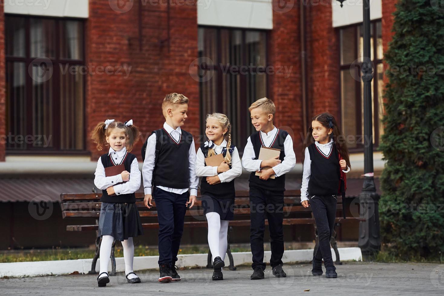 grupp av barn i skola enhetlig den där är utomhus tillsammans nära utbildning byggnad foto