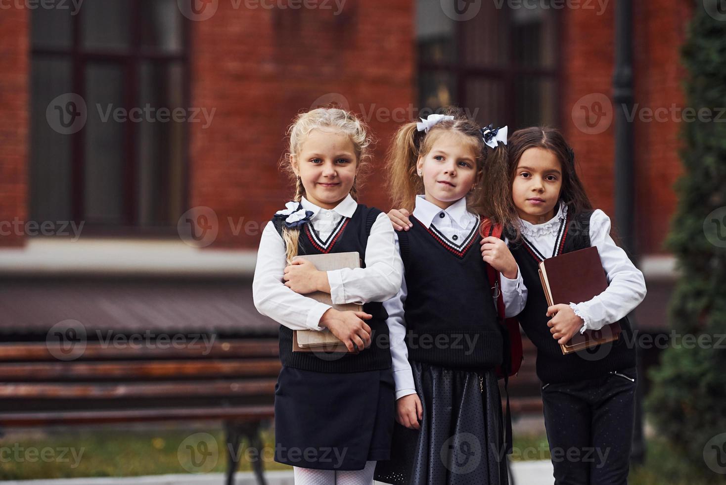 grupp av kvinna barn i skola enhetlig den där är utomhus tillsammans nära utbildning byggnad foto