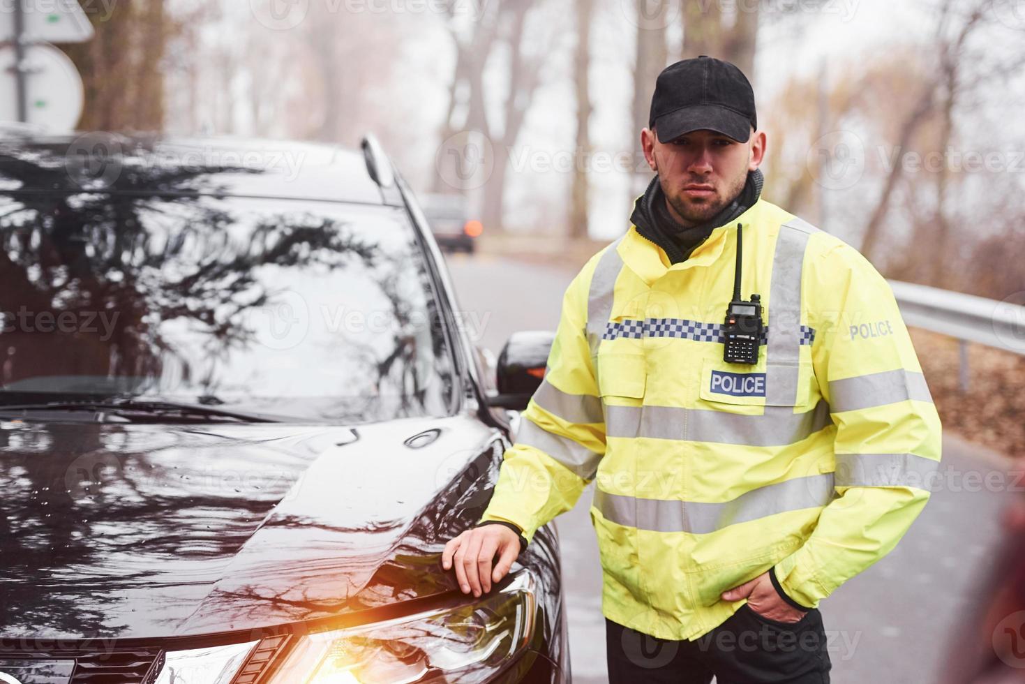 manlig polis officer i grön enhetlig stående nära fordon på de väg foto